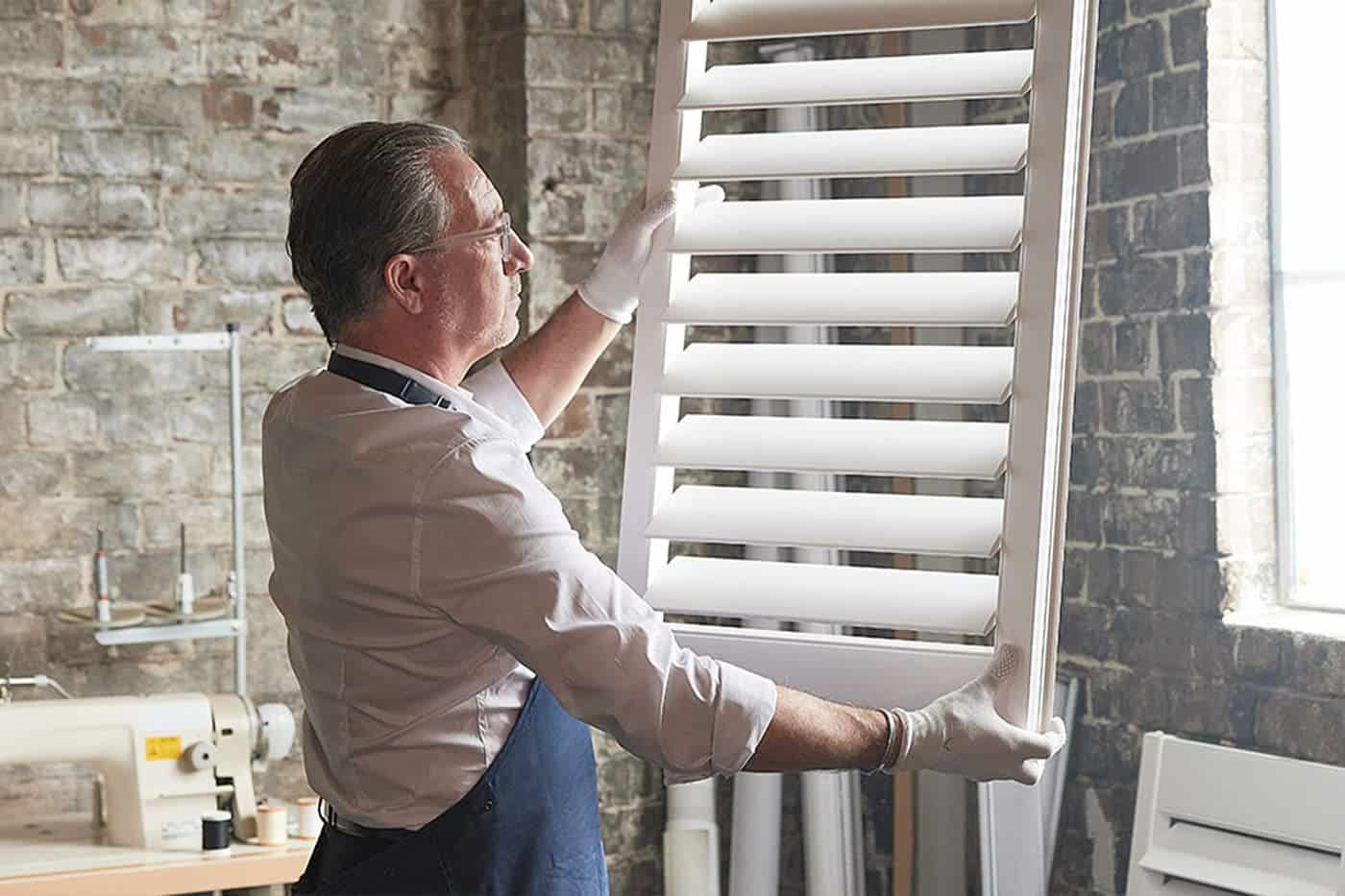 A sophisticated craftsman holding a window panel, customising to fit the window frame perfectly. Made in Australia. Available in Complete Blinds Brisbane.