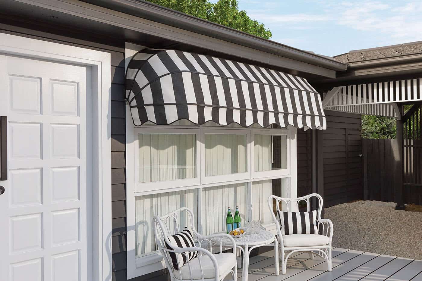 Outside view of a mid-century style home featuring Canopy Awning with black and white stripes design covering a large window pane, providing shade. Available at Complete Blinds Brisbane.
